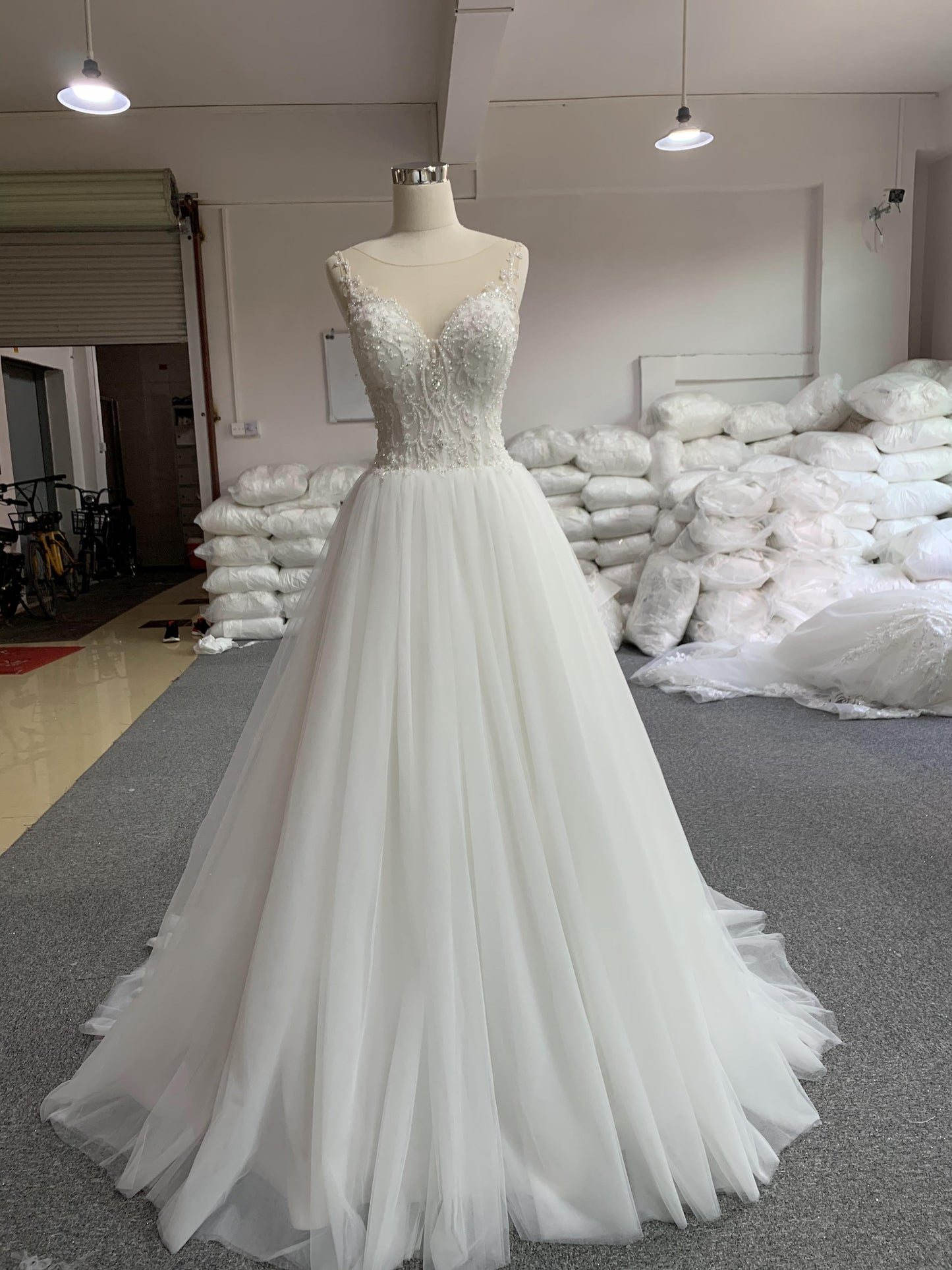 A white A-line spaghetti strap wedding dress with beaded detailing and a court train, displayed on a mannequin.
