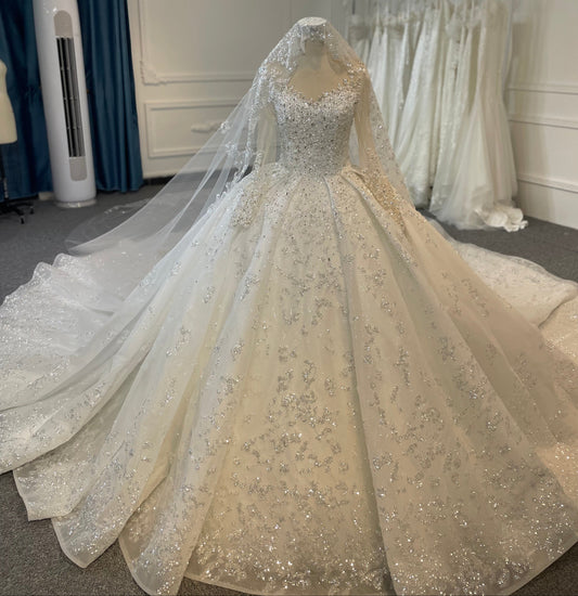 A long sleeve ball gown wedding dress with a train and 3D diamond embellishments, displayed in a bridal shop.