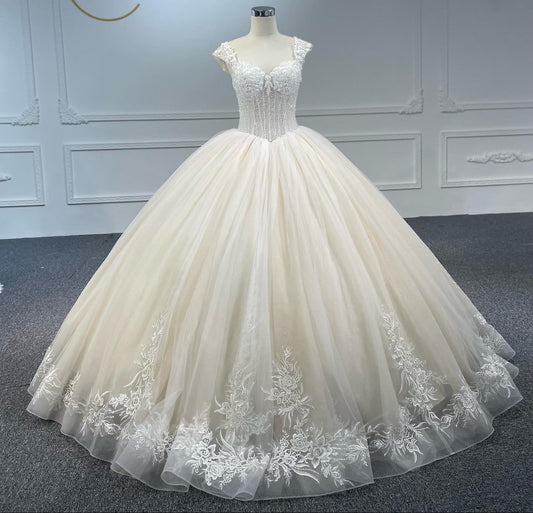 A white, sleeveless, V-neck, beaded, large canopy wedding dress with a built-in bra and back strap, displayed against a neutral background.